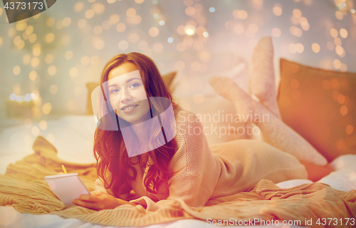 Image of happy young woman with notebook in bed at home