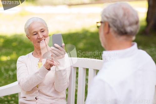 Image of old woman photographing man by smartphone in park