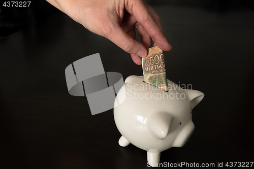 Image of Woman putting a 500 Russian Rubles bank note into a piggy bank