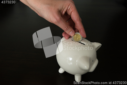 Image of Woman putting two Euro coin into a piggy bank