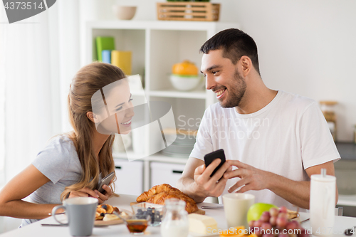 Image of couple with smartphones having breakfast at home