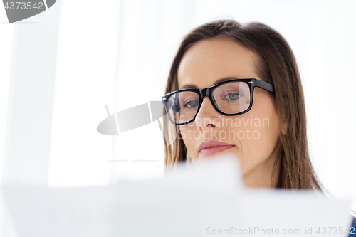 Image of businesswoman in glasses reading papers at office