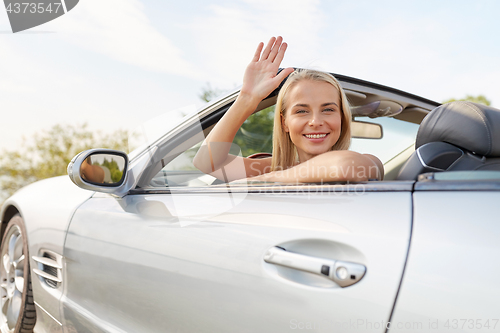 Image of happy young woman in convertible car waving hand