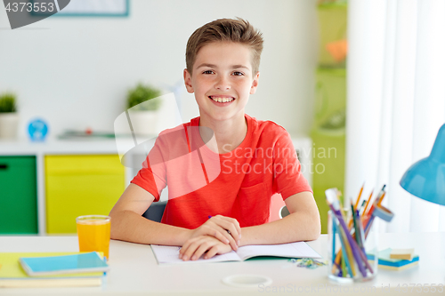 Image of happy student boy writing to notebook at home