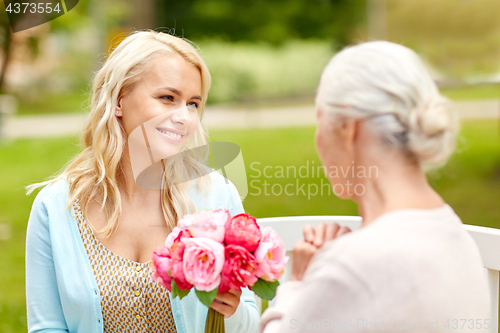 Image of daughter giving flowers to senior mother at park