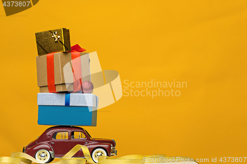 Image of Blue retro toy car delivering Christmas or New Year gifts, on yellow