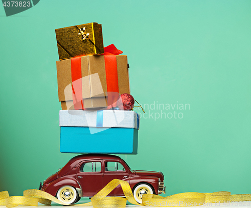 Image of Blue retro toy car delivering Christmas or New Year gifts, on yellow