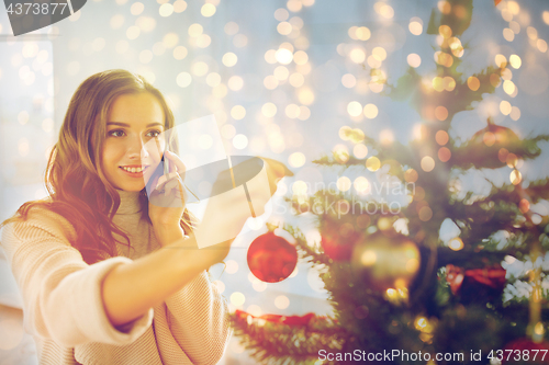 Image of woman with smartphone decorating christmas tree