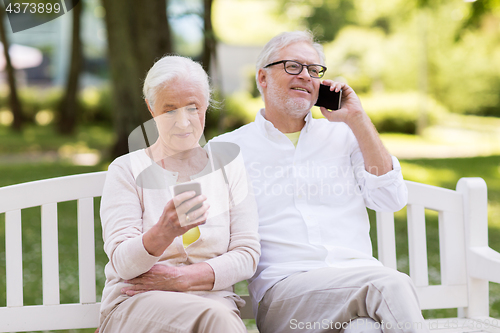 Image of happy senior couple with smartphones at park