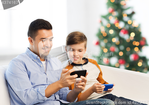 Image of happy father and son with smartphones at christmas