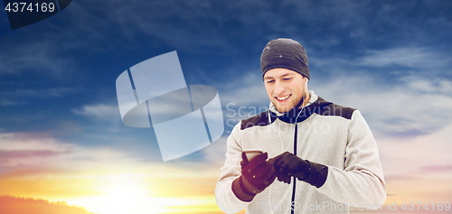 Image of happy man with earphones and smartphone in winter