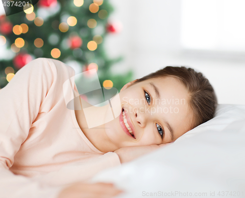 Image of happy smiling girl lying awake in bed at christmas