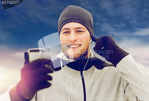 Image of happy man with earphones and smartphone in winter