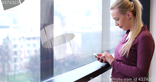 Image of Elegant Woman Using Mobile Phone by window in office building