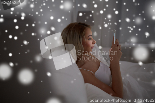 Image of young woman with smartphone in bed at home bedroom