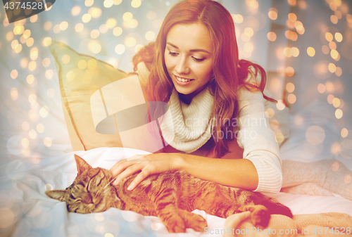 Image of happy young woman with cat lying in bed at home