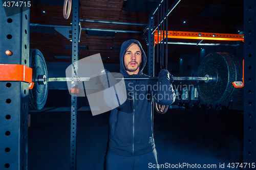 Image of Portrait of super fit muscular young man working out in gym with barbell