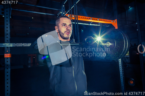 Image of Portrait of super fit muscular young man working out in gym with barbell