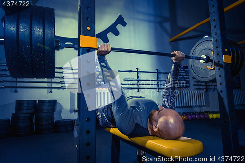 Image of Portrait of super fit muscular young man working out in gym with barbell