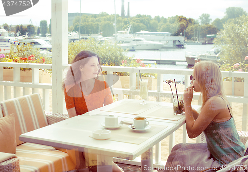 Image of portrait of two pretty modern girl friends in cafe open air interior drinking and talking, having chat and coctail, lifestyle friendship concept