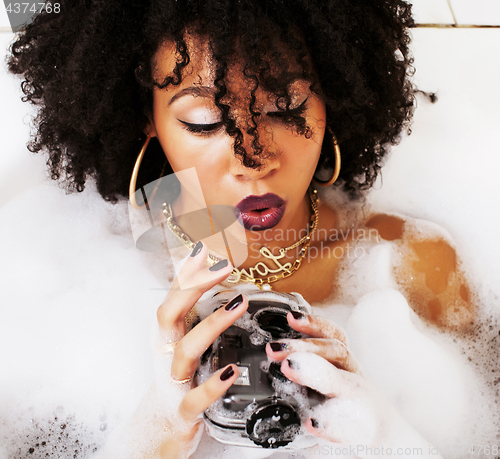 Image of young afro-american teen girl laying in bath with foam, wearing 