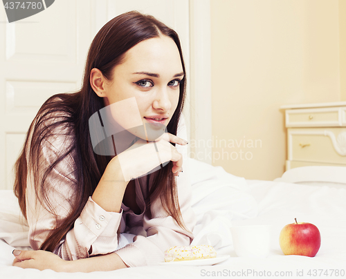 Image of young pretty brunette woman laying in bed, luxury white interior