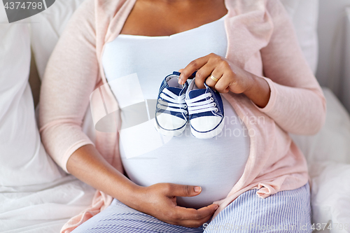 Image of pregnant african woman with baby bootees in bed