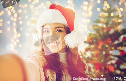 Image of happy woman in santa hat over christmas tree