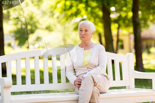 Image of sad senior woman sitting on bench at summer park