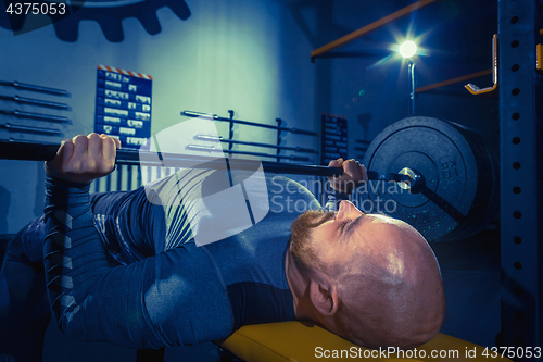 Image of Portrait of super fit muscular young man working out in gym with barbell