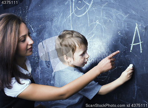 Image of little cute boy in glasses with young real teacher, classroom studying at blackboard school
