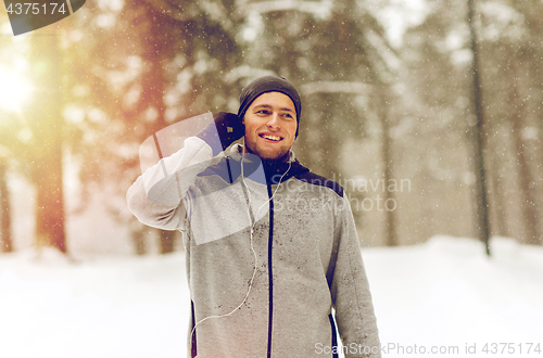 Image of happy sports man with earphones in winter forest