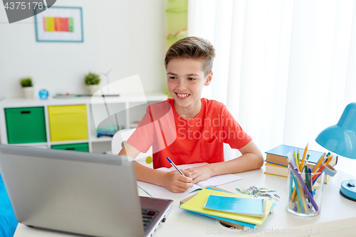 Image of student boy with laptop writing to notebook