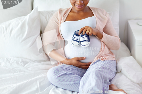 Image of pregnant african woman with baby bootees in bed