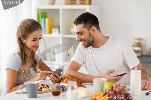 Image of couple with smartphones having breakfast at home