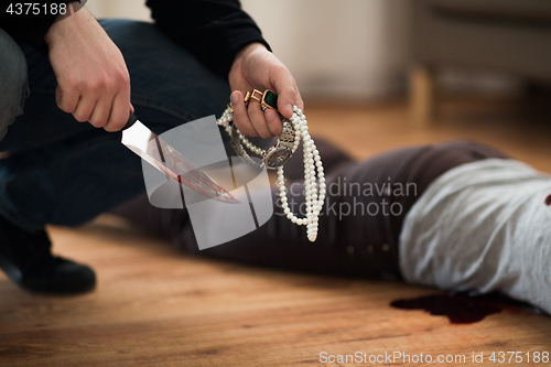 Image of criminal with knife and jewelry at crime scene