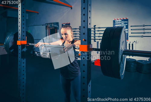 Image of Fit young woman lifting barbells looking focused, working out in a gym