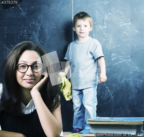 Image of little cute boy in glasses with young real teacher, classroom studying