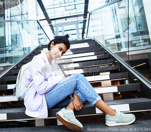 Image of young cute modern indian girl at university building sitting on stairs reading a book, wearing hipster glasses, lifestyle people concept
