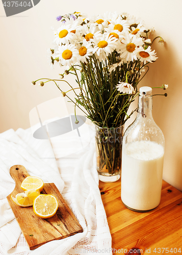 Image of Simply stylish wooden kitchen with bottle of milk and glass on table, summer flowers camomile, healthy food moring concept