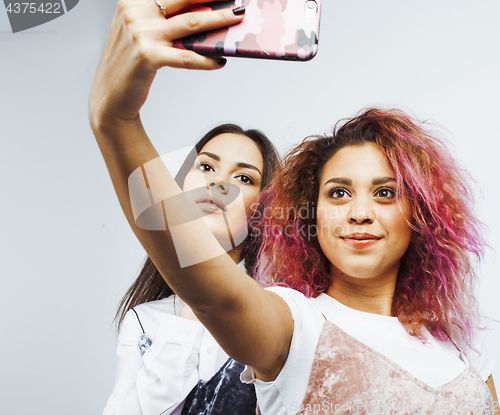 Image of lifestyle people concept: two pretty stylish modern hipster teen girl having fun together, diverse nation mixed races, happy smiling making selfie