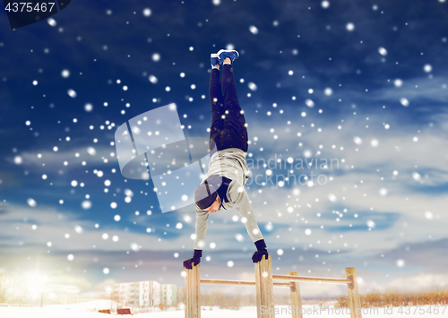 Image of young man exercising on parallel bars in winter