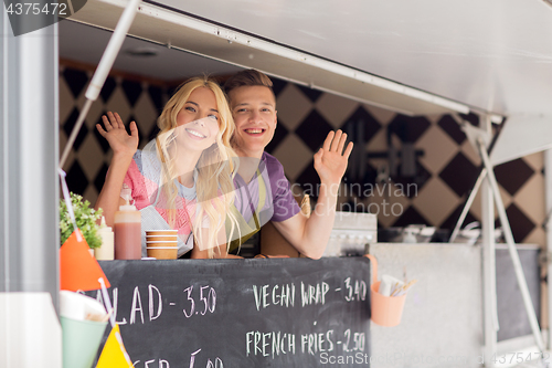 Image of happy young sellers waving hands at food truck