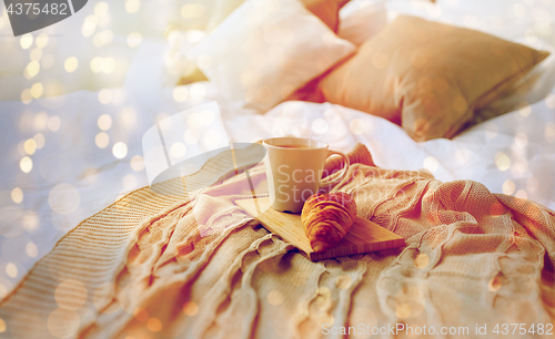 Image of coffee cup and croissant on plaid in bed at home