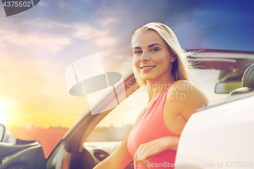 Image of happy woman in convertible car over evening sky