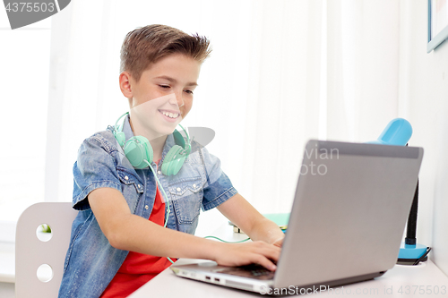 Image of happy boy with headphones typing on laptop at home