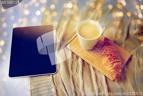 Image of tablet pc, coffee and croissant on bed at home