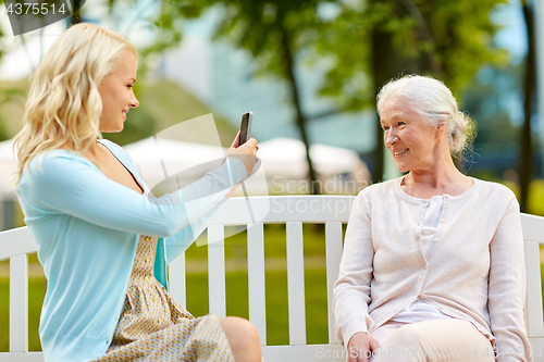 Image of daughter photographing senior mother by smartphone