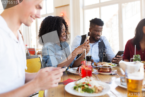 Image of happy friends with smartphones at restaurant