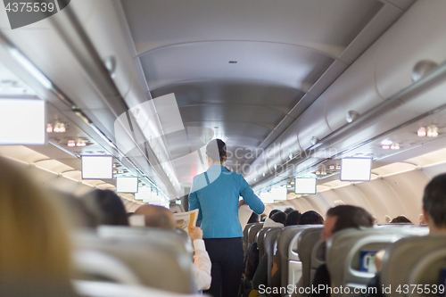 Image of Interior of commercial airplane with stewardess serving passengers on seats during flight.